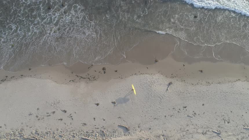 Aerial view of person with surfboard walking across beach into ocean