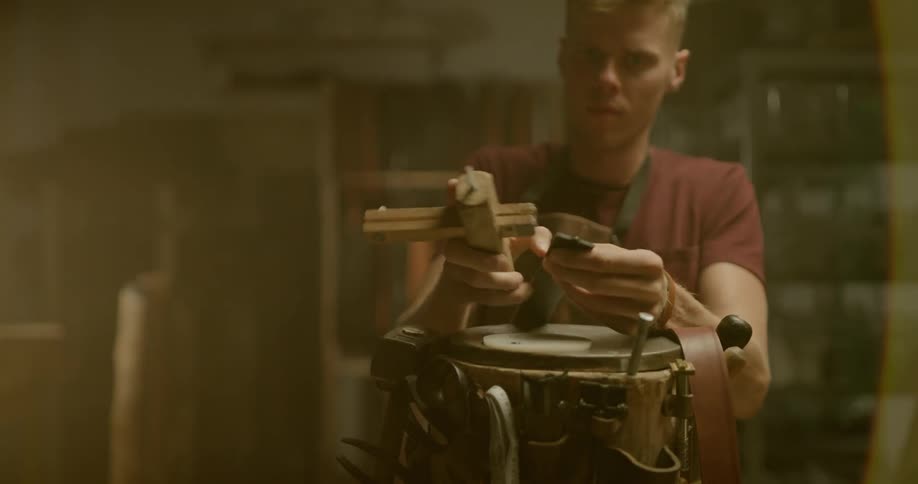 Man in apron uses tools to cut a piece of leather