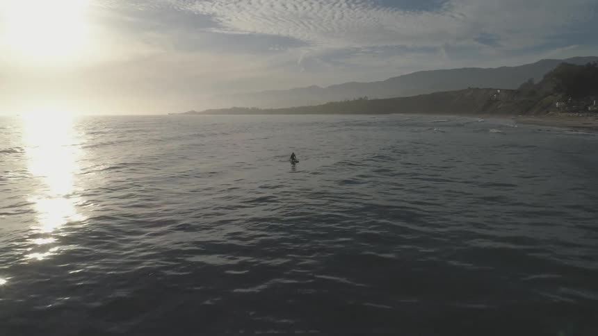Surfer rides water as sun glints down