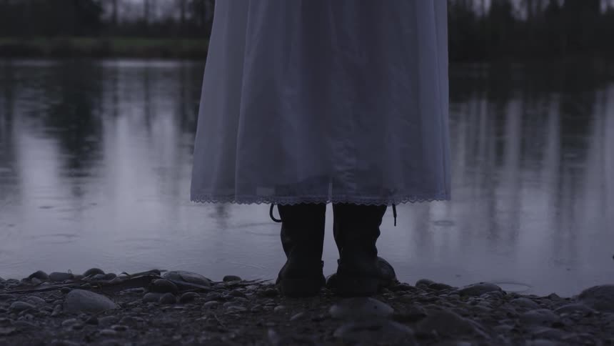 A woman in a dress standing next to a lake during the rain