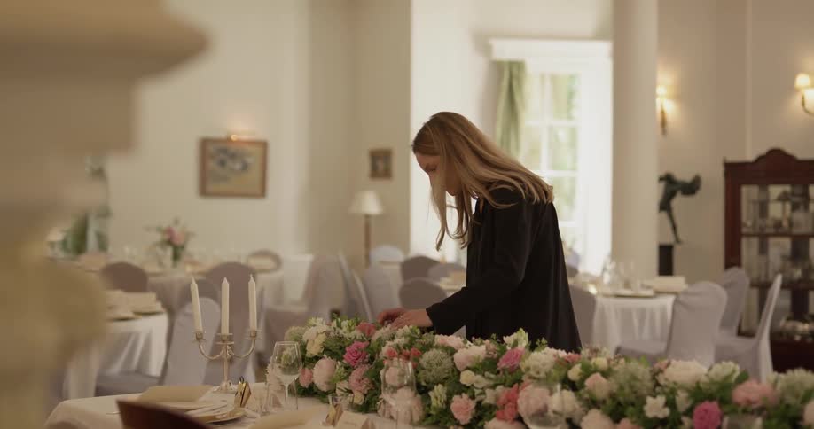 Woman touches a flower arrangement on a table