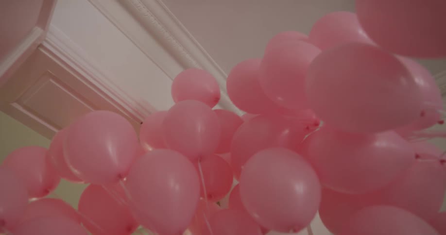 A woman holds a large amount of balloons walking into another room
