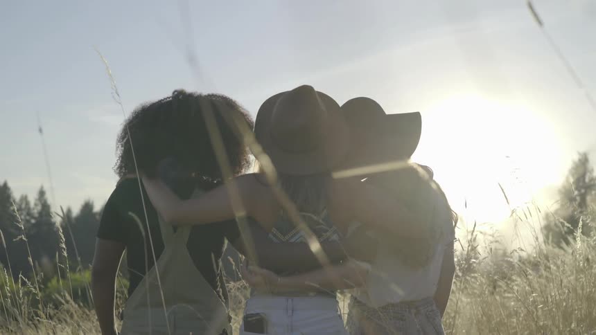 Three women hug each other in a field at noon