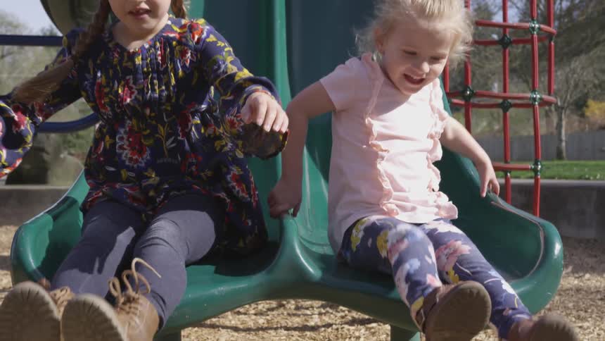 Two girls sliding down a slide at the playground