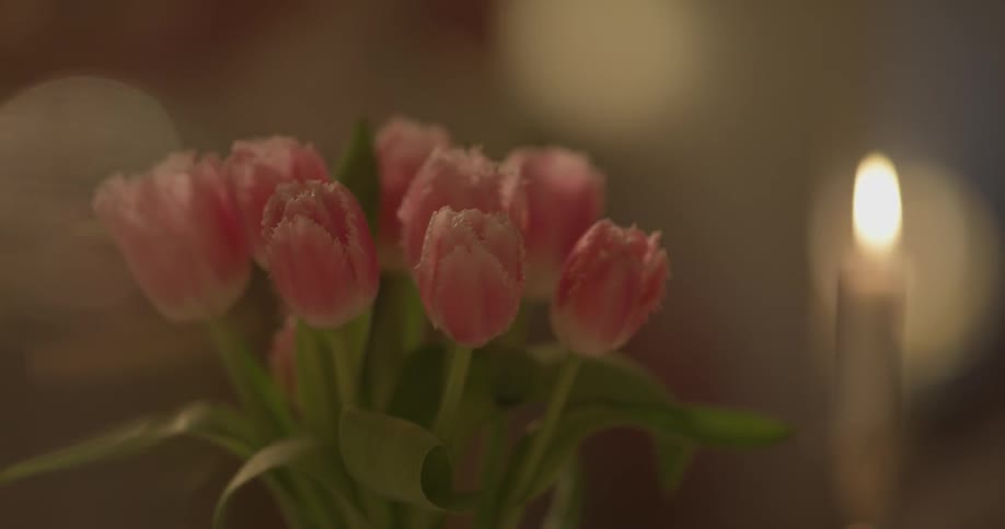 Someone sets a flower arrangement on a table by a candle