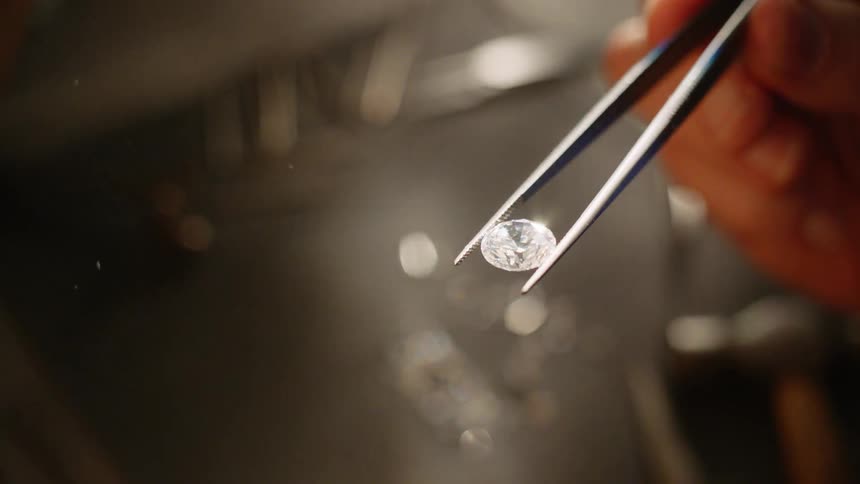 A person is picking up diamonds with a tweezer