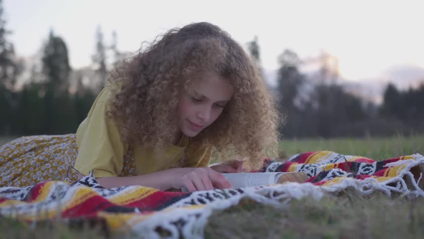 A young woman on a blanket reads a book while outdoors