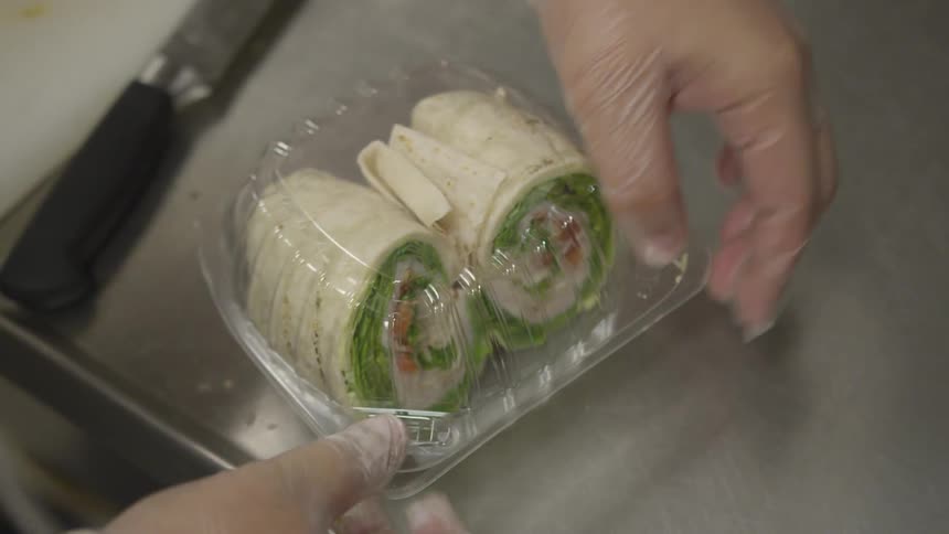 A cook wearing plastic gloves packaging a wrap