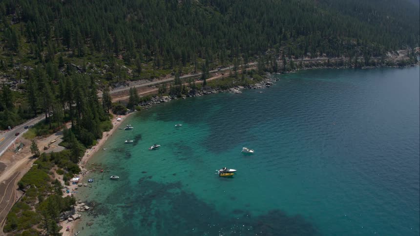 Cars drive down a highway at the bottom of a mountain next to a clear, blue ocean