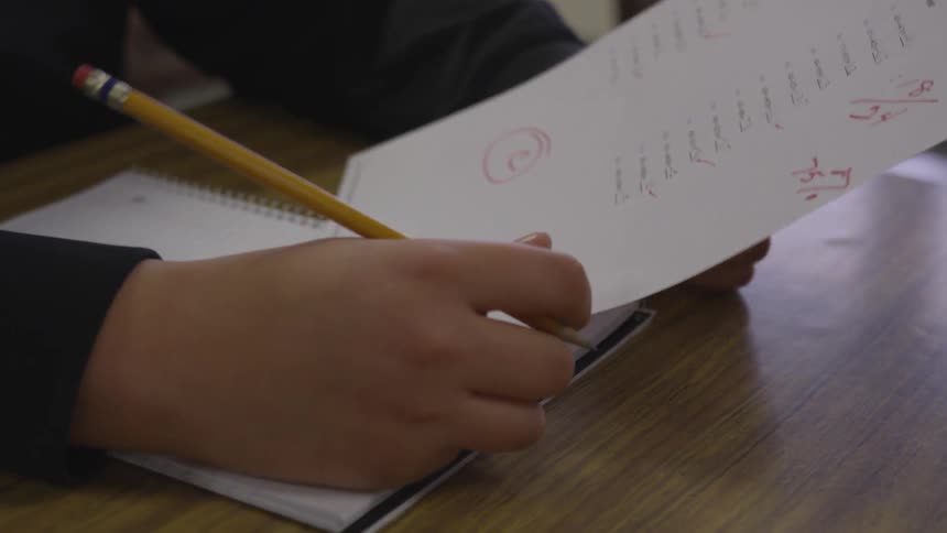 A student sits at a desk and receives a graded paper