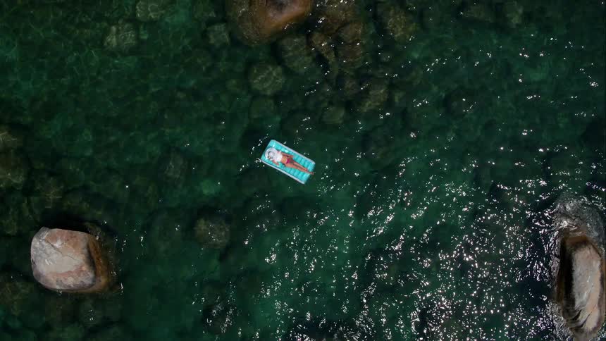 Woman is floating on raft in clear lake water on sunny day