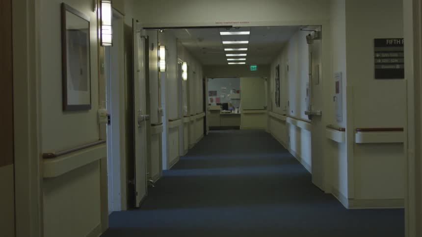 A carpeted hallway in a hospitals has many open doors