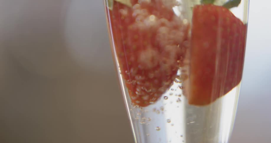 Liquid pours on top of two strawberries in a glass