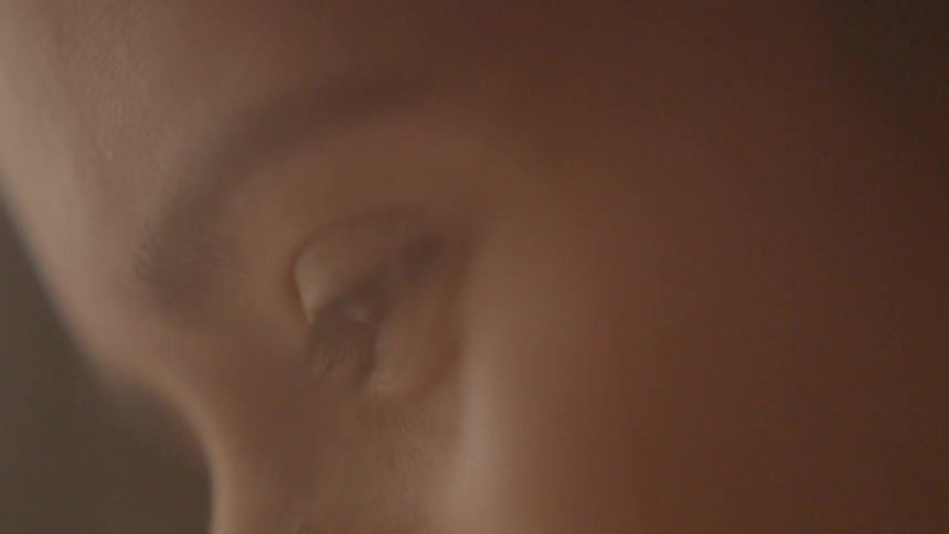 Close up of a woman's eye as she looks at something below her with interest and is smiling in a dim light room