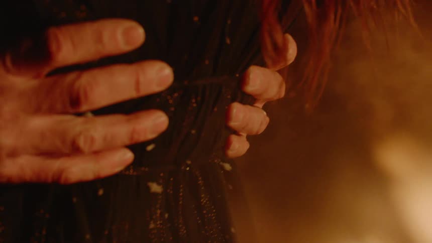 A man holds a woman around her waist with flames behind them