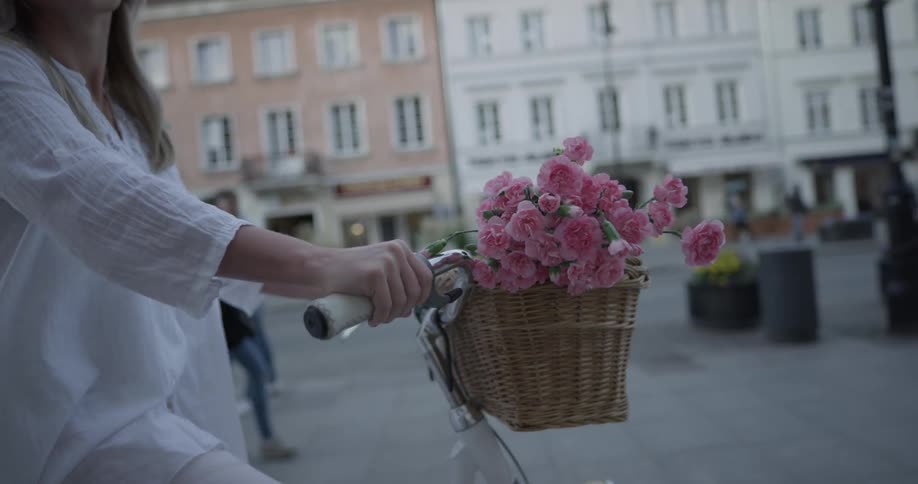 A woman rides a bike carrying flowers in a basket