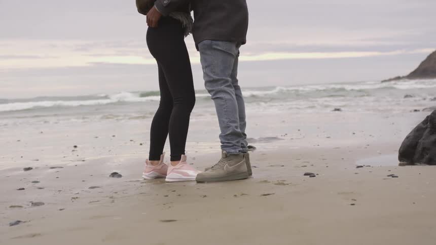 A man holds on to a woman's waist standing beside the water edge