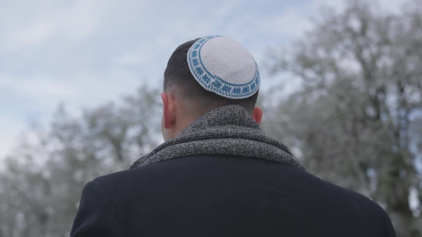 Jewish man walks alongside trees during the day