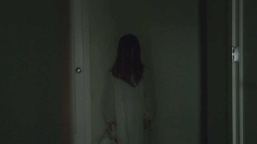 A girl in a nightgown stands in a hallway