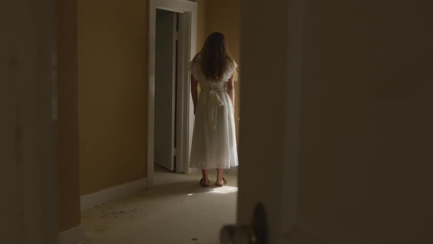A woman in a white dress standing alone in a room