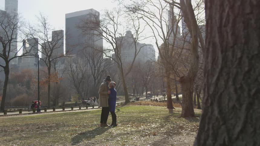 Two people stand close to each other in the park