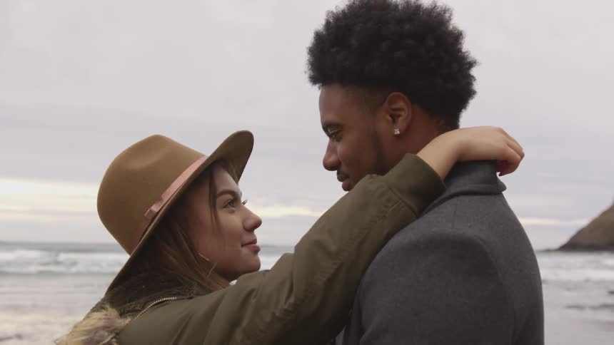 A woman stands with her arms up around a man's neck