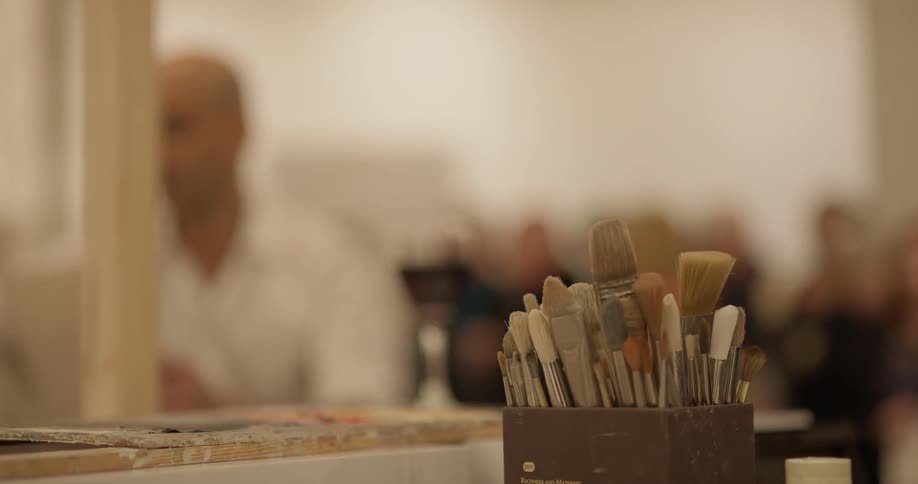Paintbrushes in focus while man paints in the background