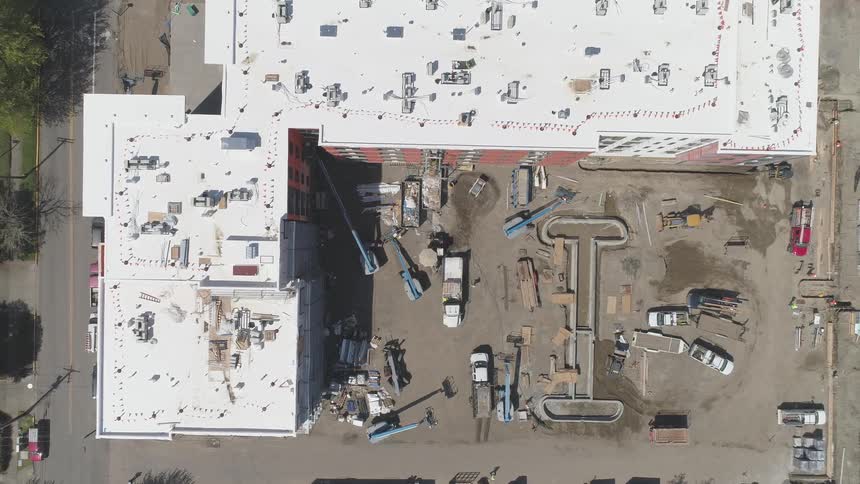 People move around a dirt parking lot in the l of a building