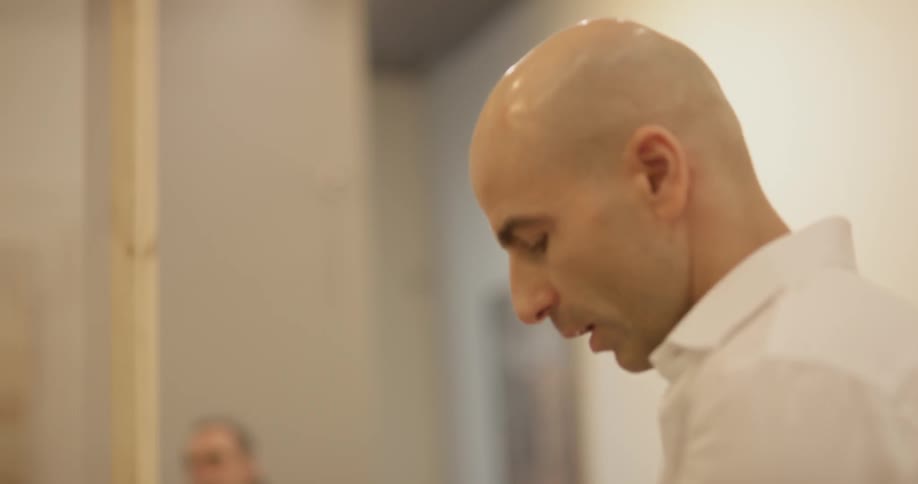 Bald man speaking in a room with cameras taking pictures of him