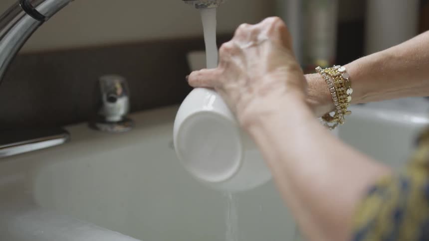 A woman washes a cup with a sponge under a kitchen sink
