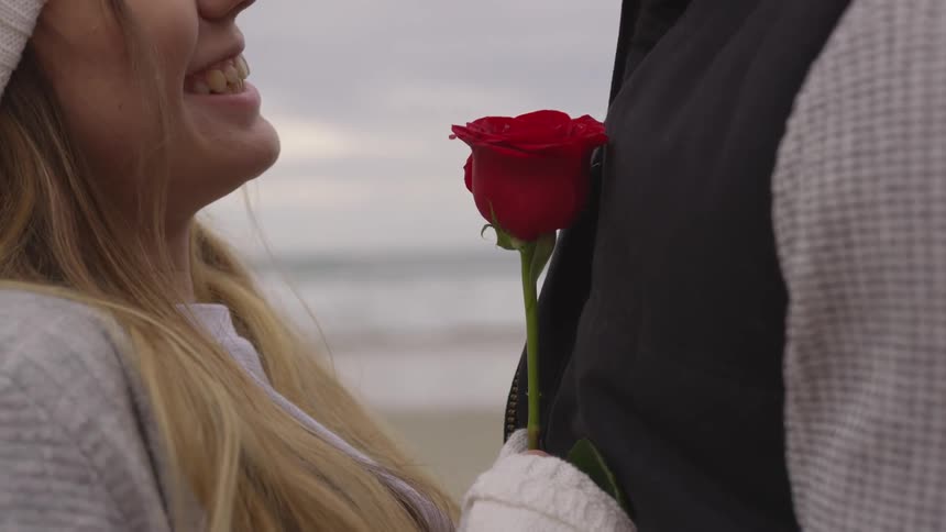 A woman smiling and holding a rose at a beach