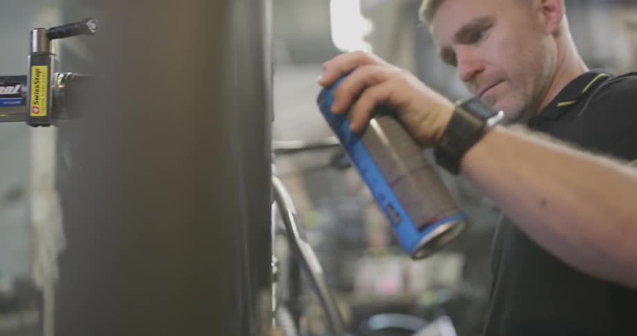 Man sprays lube on a bike tire as he turns the petal on the bicycle