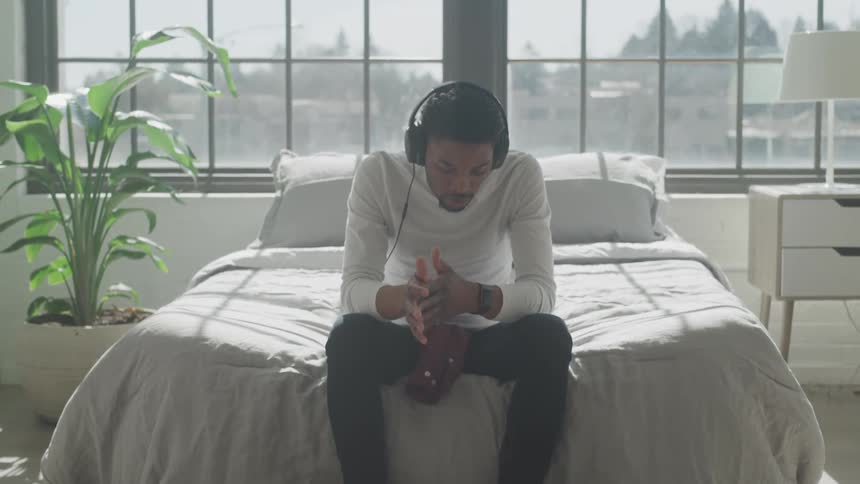 Man sitting on the end of a bed with headphones on