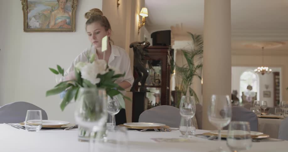 A woman places wine glasses on a table in a reception hall