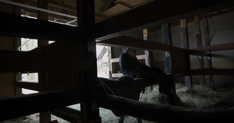 A woman places a saddle on a horse stable fence
