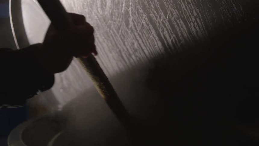 Someone stirs the contents of a large pot with a spindle as smoke emanates from the warm food