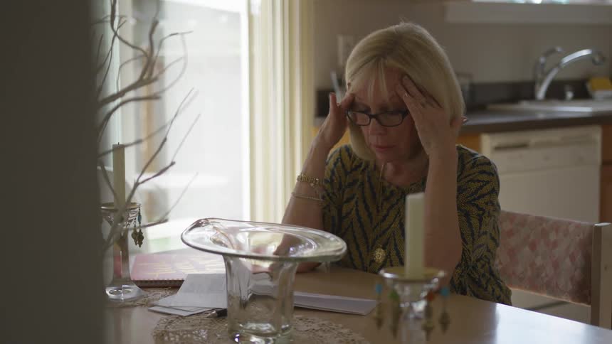 Older woman rubs forehead while sitting at table