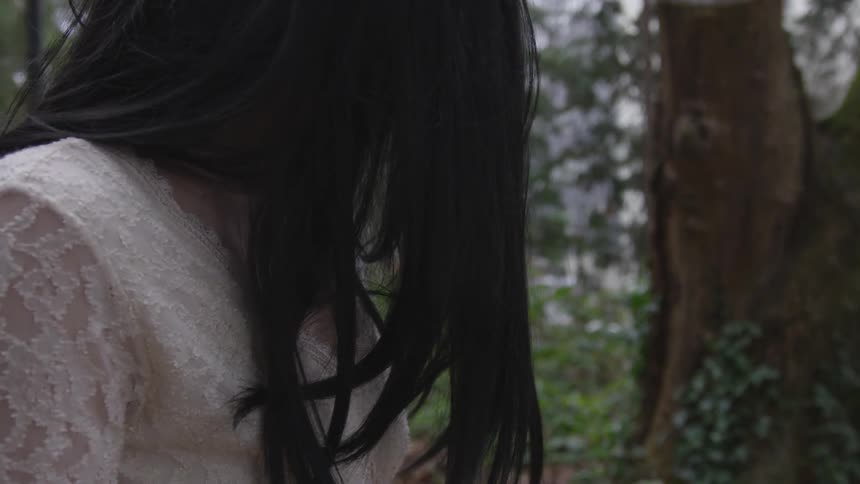 Long black hair lady women sits in the forest on a foggy day wearing a white dress looking kinda spooky like a ghost