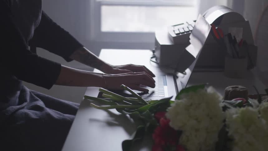 Woman working on a laptop sitting on a table with a register and bouquet of flowers