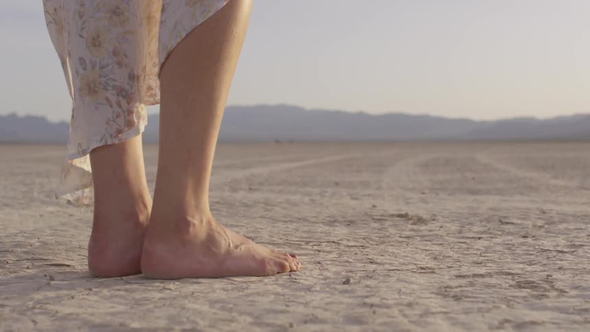 Woman stands barefoot in the desert sunset
