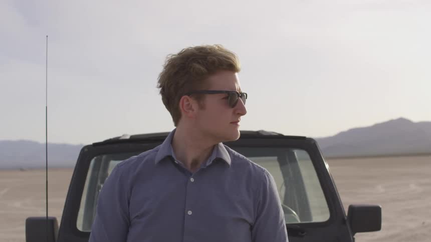 Man rests against truck hood in desert