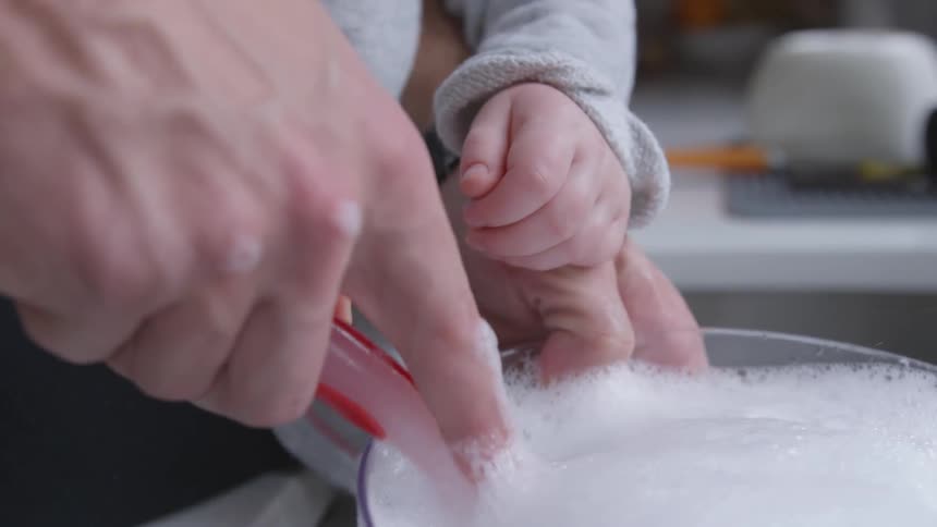 Person  stirs soapy foam with while holding child