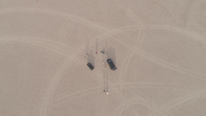 Car tracks wind through a desert with cars parked in the center