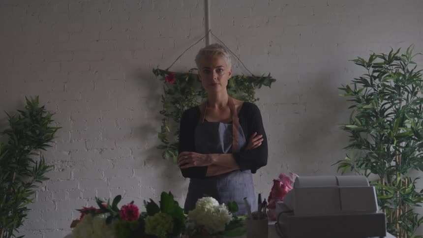 Woman stands in front of table with flowers and register and turns to camera
