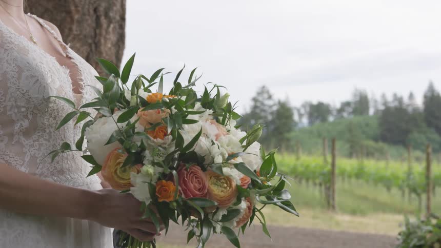 A bride walks outside at a vineyard with a bouquet of flowers