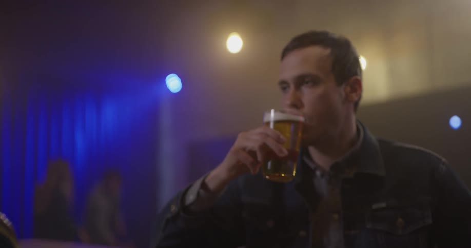 Man picks up a pint of beer at a bar and drinks it