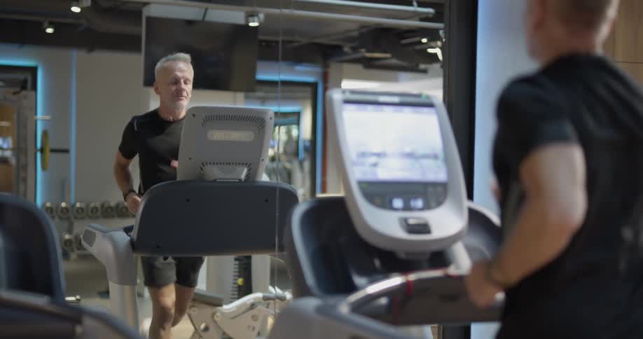Man running on a treadmill in the gym facing a mirror