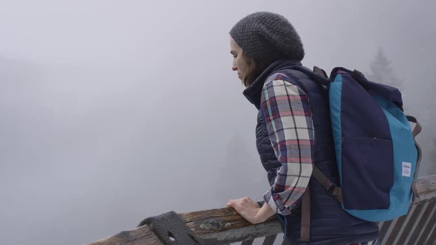 Woman leans over a wooden railing looking at the foggy woods below