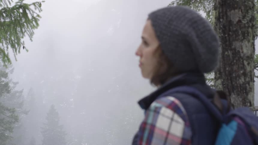 Woman wearing a backpack stands in the foggy woods