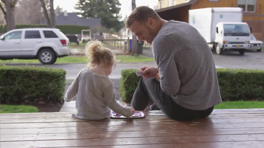 A man sits on a porch and has a tea party with a little girl